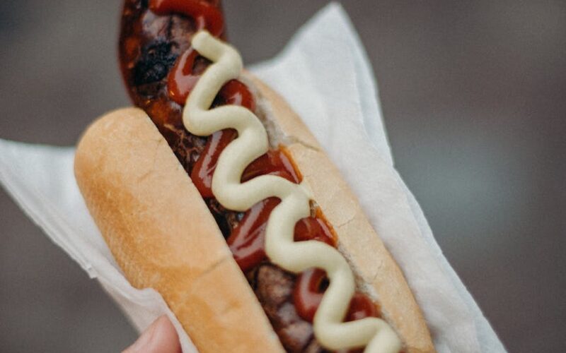 person holding hotdog sandwich with ketchup